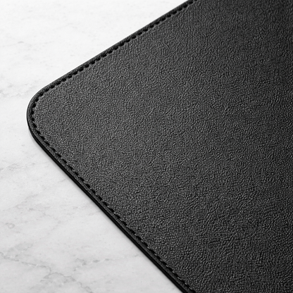 Close-up of charcoal vegan leather desk mat corner showing textured surface and stitched edge.