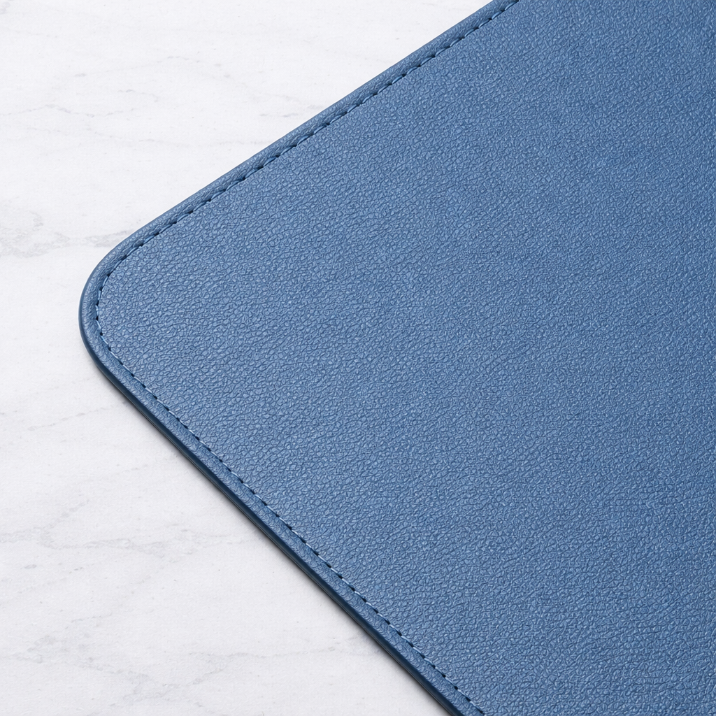 Close-up of deep blue vegan leather desk mat corner showing textured surface and stitched edge.