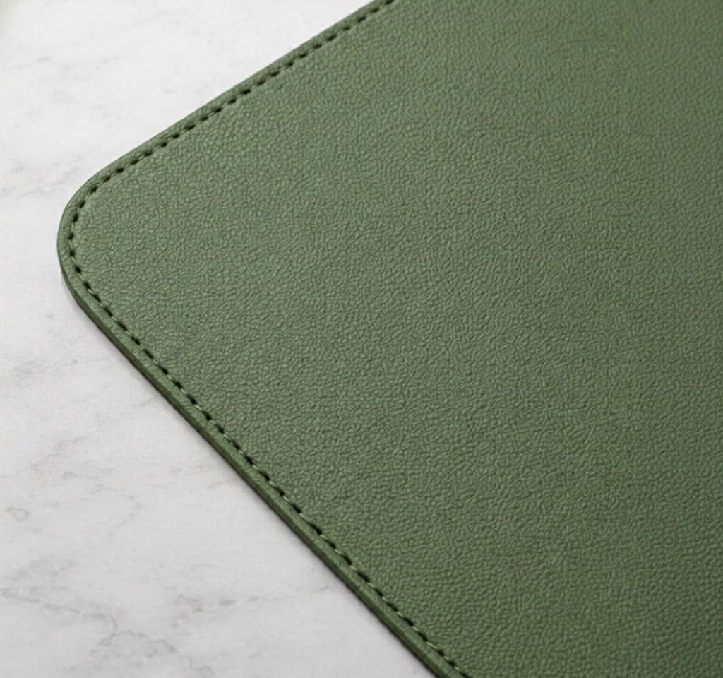 Close-up of eucalyptus green vegan leather desk mat corner showing textured surface and stitched edge.