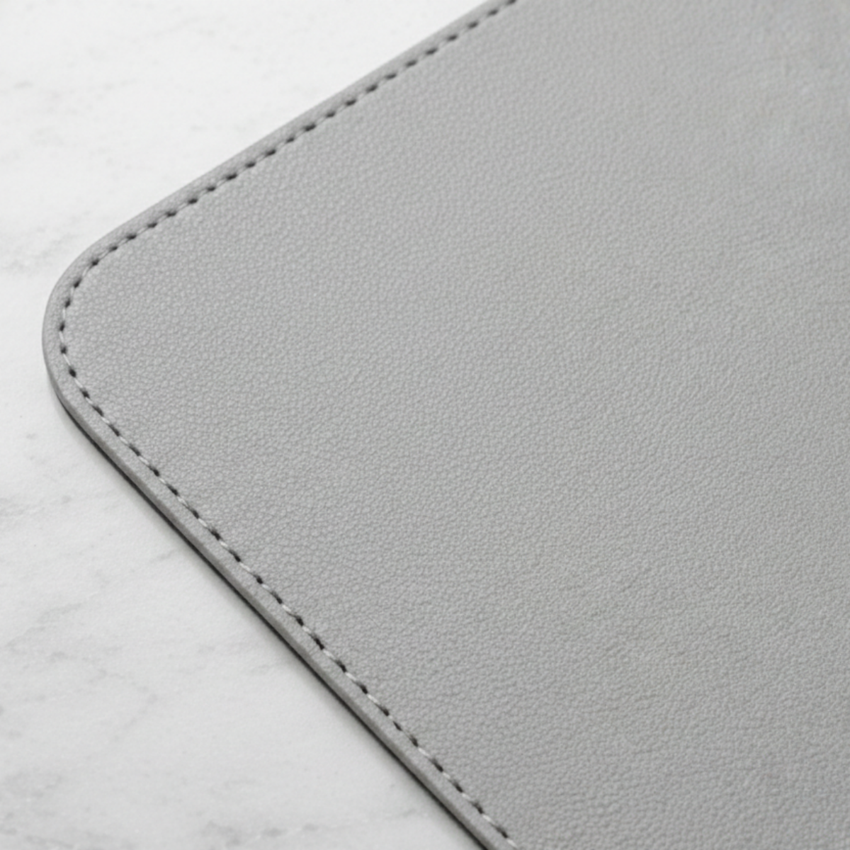 Close-up of stone gray vegan leather desk mat corner showing textured surface and stitched edge.
