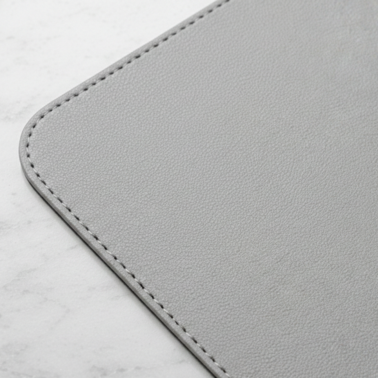 Close-up of stone gray vegan leather desk mat corner showing textured surface and stitched edge.

