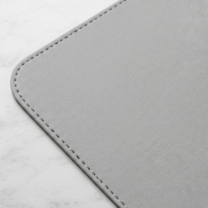 Close-up of stone gray vegan leather desk mat corner showing textured surface and stitched edge.
